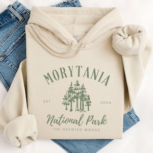 May include: A beige hoodie with a green graphic design that says "Morytania National Park The Haunted Woods" with the text "EST 2004" underneath the graphic.