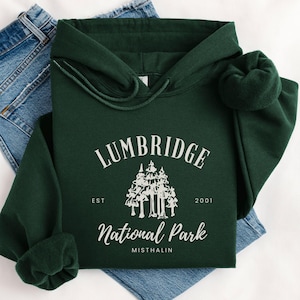 May include: A dark green hooded sweatshirt with a white graphic design that says "Lumbridge National Park Est 2001 Misthallin". The graphic features a stylized image of a group of trees.