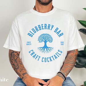 May include: White t-shirt with a blue circular graphic that reads "Blurberry Bar Craft Cocktails" around a tree design. The shirt also includes the text "Finest Quality" and "Since 2002".