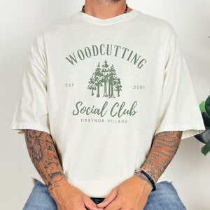May include: A white t-shirt with a green logo that says "Woodcutting Social Club" with the text "Est. 2001" and "Draynor Village" underneath.