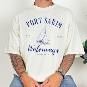 May include: A white t-shirt with a blue graphic of a sailboat and the text "Port Sarim Waterways Asgarnia Est 2001".