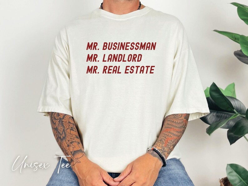 Puede incluir: Camiseta unisex color crema con las frases "MR. BUSINESSMAN", "MR. LANDLORD" y "MR. REAL ESTATE" impresas en rojo. La camiseta tiene mangas cortas y un corte holgado. Las palabras "Unisex Tee" est&aacute;n escritas en cursiva en la parte inferior.