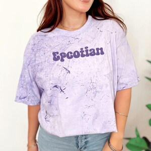 May include: A purple tie-dye t-shirt with the text "Epcotian" in a retro purple font.