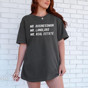 Puede incluir: Camiseta unisex gris oscuro con las frases blancas "MR. BUSINESSMAN", "MR. LANDLORD" y "MR. REAL ESTATE". La camiseta es de estilo casual, adecuada para el uso diario. Las palabras "Unisex Tee" est&aacute;n escritas en cursiva en la parte inferior.