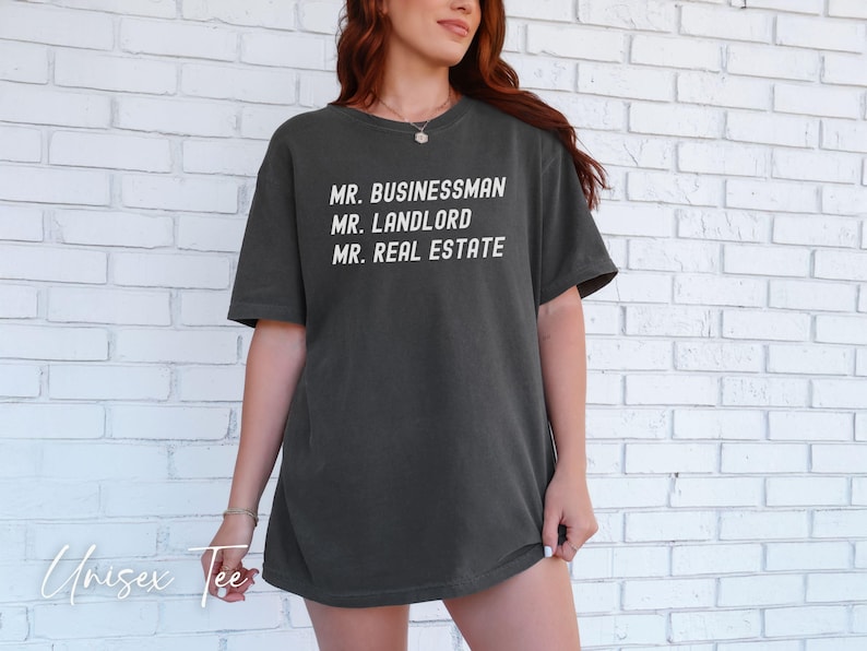Puede incluir: Camiseta unisex gris oscuro con las frases blancas "MR. BUSINESSMAN", "MR. LANDLORD" y "MR. REAL ESTATE". La camiseta es de estilo casual, adecuada para el uso diario. Las palabras "Unisex Tee" est&aacute;n escritas en cursiva en la parte inferior.