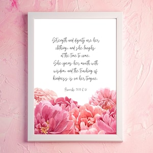 May include: A white framed print with a pink floral design and a quote from Proverbs 31:25 & 26: "Strength and dignity are her clothing, and she laughs at the time to come. She opens her mouth with wisdom, and the teaching of kindness is on her tongue."