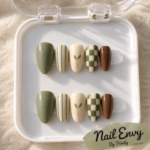 May include: A set of ten almond-shaped press-on nails in a white plastic case. The designs include solid olive green, cream with vertical green stripes, cream with a small green sprout graphic, a green and cream checkerboard, and solid brown.