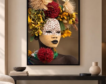 Könnte beinhalten: Ein gerahmter Kunstdruck mit dem Porträt einer dunkelhäutigen Person, die einen großen Blumenschmuck aus roten, gelben und beigen Blüten trägt. Das Gesicht ist mit weißen kreisförmigen Mustern und einer beigen Maske sowie dunklen Lippen verziert.