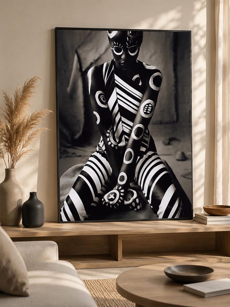 May include: A framed black and white wall art print featuring a person with dark skin adorned in intricate white body paint patterns, including circular motifs, diagonal stripes, and geometric shapes, captured in a seated, forward-facing pose.