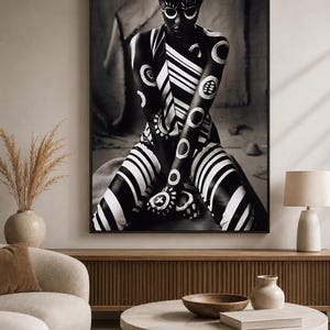 May include: A framed wall art print featuring a high-contrast black and white photograph of a figure adorned with intricate white circular and striped body paint patterns, posed in a seated position with arms crossed over the knees.