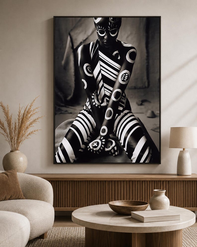 May include: A framed wall art print featuring a high-contrast black and white photograph of a figure adorned with intricate white circular and striped body paint patterns, posed in a seated position with arms crossed over the knees.