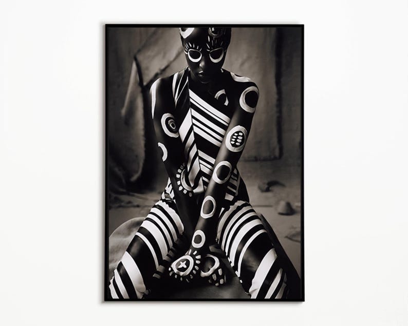 May include: A black and white photographic print featuring a figure adorned with bold, high-contrast patterns. The design includes circular motifs, thick diagonal stripes, and intricate markings across the skin, presented in a vertical frame.