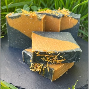 May include: Three bars of handmade soap with a black and orange swirl design. The soap is decorated with dried flower petals.