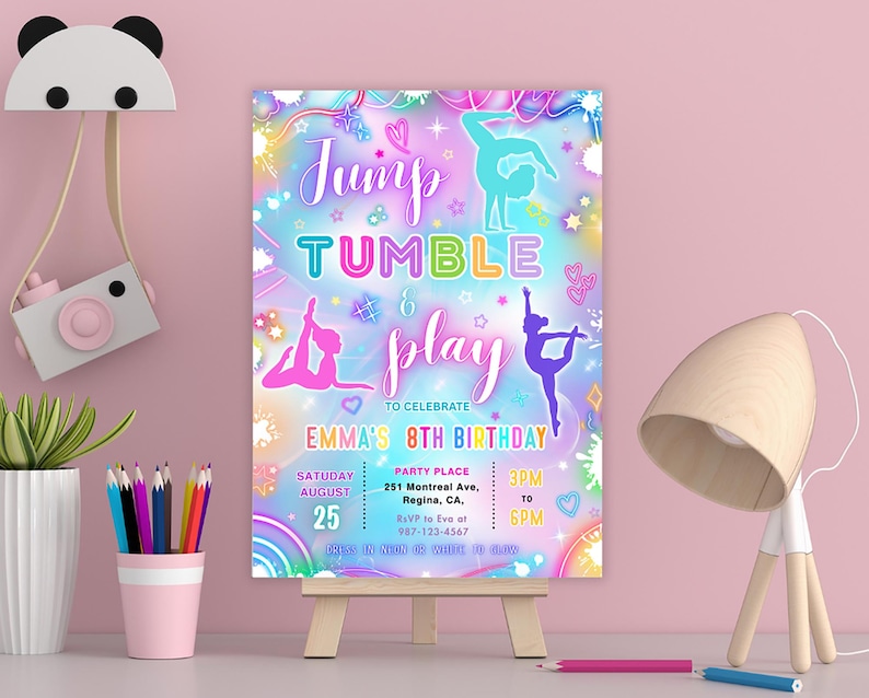 May include: A colorful gymnastics-themed birthday party invitation. The design features the words "Jump, Tumble & Play" with gymnast silhouettes and event details. The invitation is displayed on a small wooden easel.