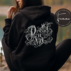 May include: Black hoodie with the text "Pretty n Ink" in a decorative, swirling font on the back. The hoodie also features a logo that says "Original Femme Apparel".
