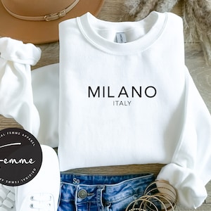 May include: White crewneck sweatshirt with the text "MILANO ITALY" printed in black on the front.