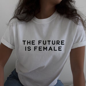 以下が含まれることがあります： 「THE FUTURE IS FEMALE」という黒い文字が書かれた白いTシャツです。