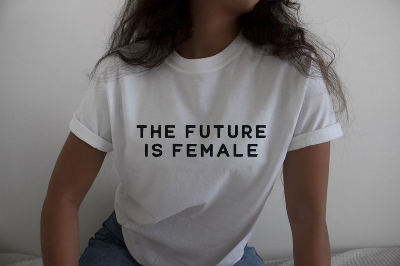 以下が含まれることがあります： 「THE FUTURE IS FEMALE」という黒い文字が書かれた白いTシャツです。