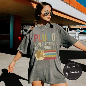 May include: A gray t-shirt with a vintage-style graphic that says "Pluto Never Forget 1930-2006" with a yellow moon and rainbow stripes. The shirt is made by Original Femme Apparel.