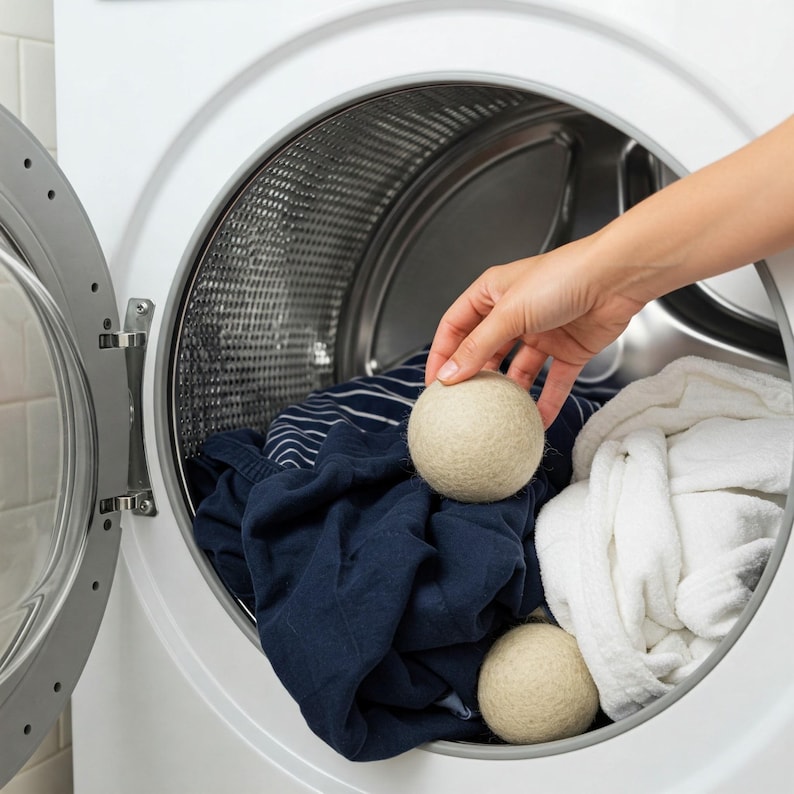 Peut inclure: Deux balles de s&eacute;chage en laine beige &agrave; l'int&eacute;rieur d'un tambour de machine &agrave; laver blanc avec une chemise ray&eacute;e bleu et blanc et une serviette blanche.
