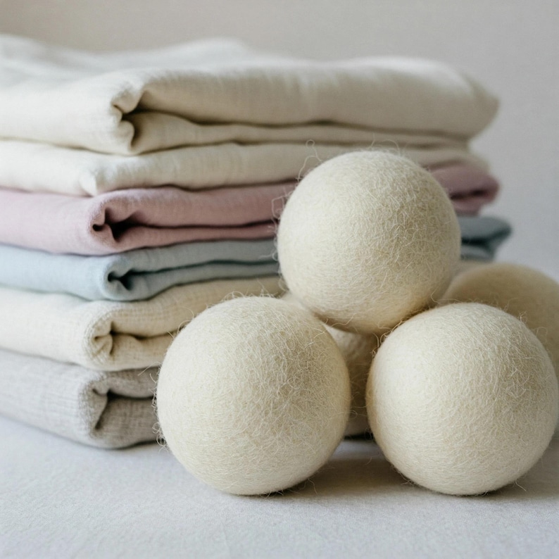 Peut inclure: Quatre boules de s&eacute;chage en laine blanche empil&eacute;es sur une pile de tissu blanc, rose, bleu et beige pli&eacute;.