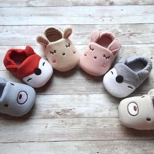 May include: Six pairs of baby booties with animal faces. The booties are made of soft, plush fabric and come in a variety of colors, including red, pink, gray, and beige.