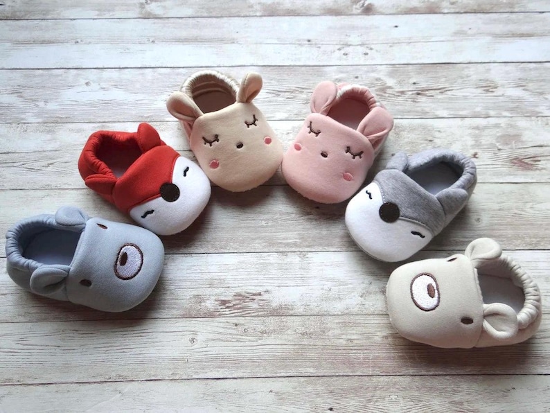 May include: Six pairs of baby booties with animal faces. The booties are made of soft, plush fabric and come in a variety of colors, including red, pink, gray, and beige.