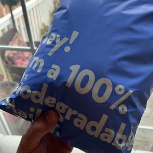Peut inclure: Un sac d'exp&eacute;dition en plastique bleu avec le texte "Hey! I'm a 100% biodegradable" imprim&eacute; en blanc.