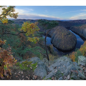 Könnte beinhalten: Panoramablick von einer felsigen Klippe auf einen gewundenen Fluss in einem Wald. Die Bäume sind eine Mischung aus Grün und Gelb, was auf den Herbst hindeutet. Der Fluss ist tiefblau und der Himmel ist hellblau mit einigen Wolken.