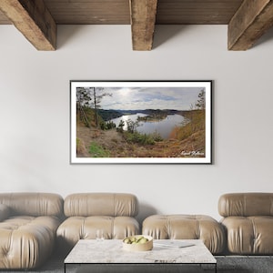 Könnte beinhalten: Ein gerahmtes Foto einer malerischen Landschaft mit einem See, der von Bäumen umgeben ist. Der See ist in der Ferne und die Bäume im Vordergrund. Das Foto hängt an einer weißen Wand in einem Wohnzimmer.