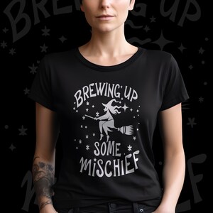 May include: Black t-shirt with a white graphic of a witch flying on a broomstick with the text "Brewing Up Some Mischief".