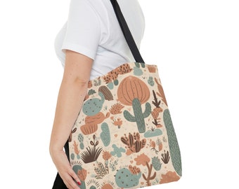 May include: Tote bag with a desert-themed pattern. The design features various cacti, succulents, and desert plants in shades of green, brown, and peach on a cream background. The bag has a black strap.