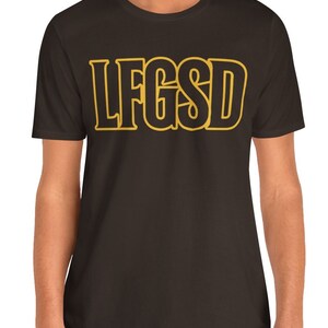 Puede incluir: Una camiseta marrón oscuro con un contorno amarillo del texto "LFGS" en la parte delantera.
