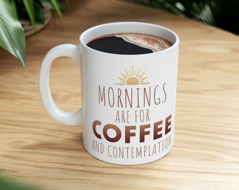 May include: White ceramic coffee mug with a black handle. The mug has a gold sun graphic and the text "Mornings are for Coffee and Contemplation" in brown text.
