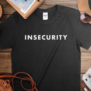 May include: A dark gray t-shirt with the word "INSECURITY" printed in white on the front.