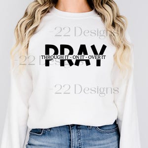 Op de afbeelding: Witte longsleeve trui met zwarte tekst die "Pray Through It - On It - Over It" luidt.