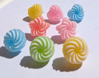 Könnte beinhalten: Eine Sammlung bunter, spiralförmiger Süßigkeiten in verschiedenen Formen, darunter Herzen, Sterne und Kugeln. Die Süßigkeiten sind in Gelb-, Rosa-, Blau- und Grüntönen mit weißen Akzenten gehalten. Sie sind auf einer weißen Oberfläche angeordnet.
