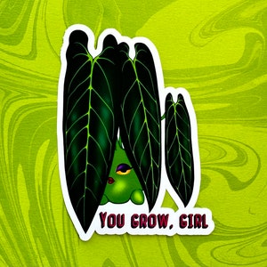 May include: A green plant with large, dark green leaves and a cartoon face peeking out from behind the leaves. The text "YOU GROW, GIRL" is written in pink below the plant.