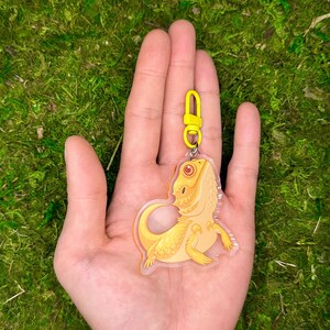 May include: A yellow bearded dragon keychain made of clear acrylic with a yellow metal clasp.