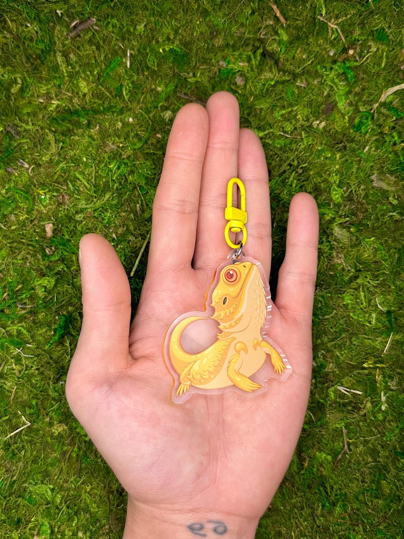 May include: A yellow bearded dragon keychain made of clear acrylic with a yellow metal clasp.
