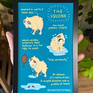 May include: A framed print featuring a cartoon illustration of "The Squonk," a small, wrinkly creature with warts and loose skin, crying. The text describes the creature as the most pathetic cryptid. The background is teal.