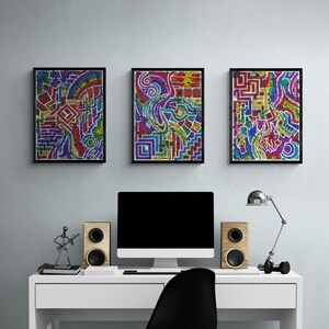 May include: Three framed abstract art prints with colorful geometric designs hang above a white desk. The desk holds a computer, speakers, a lamp, and a black chair with wooden legs. The artwork features red, blue, yellow, and green hues.