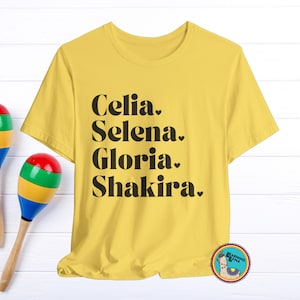 May include: Yellow t-shirt with the names Celia, Selena, Gloria, and Shakira printed in black. Two maracas with red, green, yellow, and blue accents are on the left. A round sticker with a llama is on the bottom right.