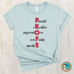 May include: A light blue t-shirt with the word "PROFE" spelled vertically in colorful letters. The word is an acronym for qualities like "patient" and "creative". The shirt has rolled-up sleeves and a small circular sticker.