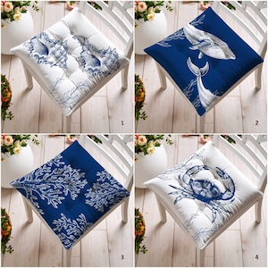 Może przedstawiać: Cztery kwadratowe poduszki na siedzenia z motywami morskimi. Poduszki mają kolory biały i granatowy, z ilustracjami muszli, wielorybów, koralowców i kraba. Każda poduszka jest umieszczona na białym krześle.