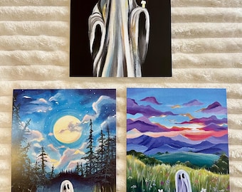 May include: Three paintings featuring ghost figures. One shows a ghost holding a candle against a black background. The other two depict ghosts in colorful landscapes: one under a full moon, the other in a field with a sunset.