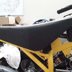 Może przedstawiać: Żółty mini motocykl z czarnym siedzeniem i czarnym kierownicą. Motocykl ma czarny amortyzator i czarną oponę.