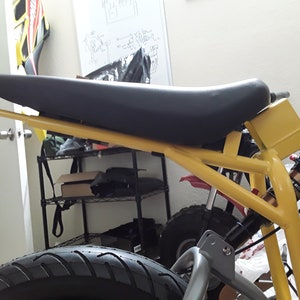 May include: A yellow metal frame with a black padded seat. The frame has a black rear tyre and a black shock absorber.