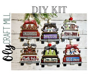 May include: Six wooden Christmas truck ornaments with different designs. The trucks are red, white, and black with various holiday themes, including gingerbread, baby it's cold, Henry & Bright, North Pole, Tree & Farm, and let it snow.