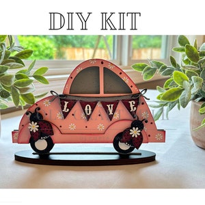 May include: DIY kit for a pink wooden car with ladybug accents and a banner that says "LOVE".